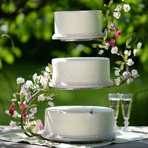 Three-tiered wedding cake with floral decorations on a table outdoors.